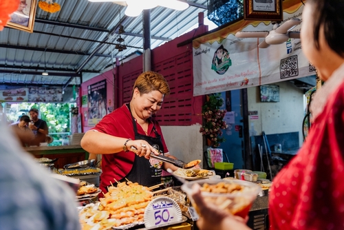 Smiling woman vendor selling local food at food stall at Khlong Lat Mayom market. Thai street food, Bangkok, Thailand