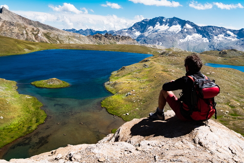 Trekker takes a rest looking at mountain panorama, sitted on a rock, summer sunny day. Gran Paradiso National Park, Western italian Alps, Italy