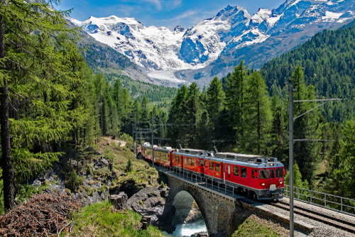 The Bernina Express train travels along the lake shore of Lago Bianco and Piz Cambrena near Milano, Lombardy, Italy