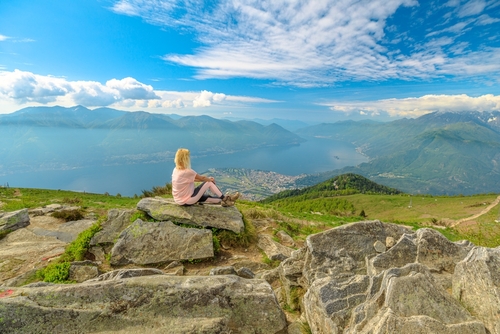 Relaxing woman taking a break after trekking, sitting on top of Cardada-Cimetta mount in Switzerland. Skyline from Swiss chairlift of Locarno on Cardada mount. Lake Langensee cityscape in Ticino.