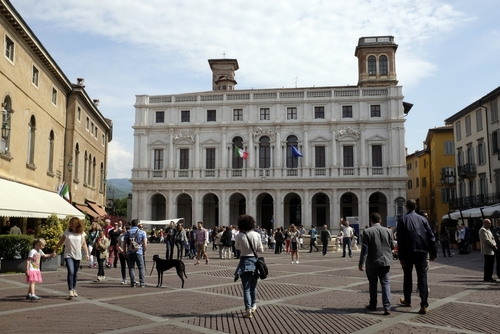 People walking around Piazza Vecchia with Palazzo della Ragione in the background in Bergamo, Lombardy, Italy