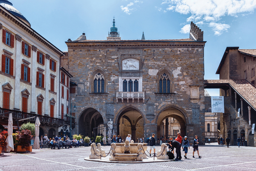 People walking around and sitting in restaurants near the building of the Cathedral Museum and Treasury (Museo Del Tesoro Della Cattedrale) on the Piazza Vecchia street in Upper Bergamo (Citta Alta), Lombardy, Italy