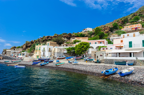 Tourists walking around colorful houses and a beautiful beach with fishermen boats on the island of Alicudi, Aeolian Islands, near Sicily, Italy