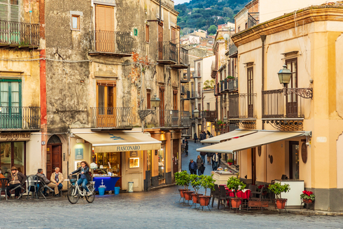 Bicyclist riding past cafes in the beautiful Piazza of Castelbuono near Cefalu, Palermo, Sicily, Italy