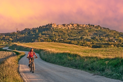 Nice senior woman riding her electric mountain bike in the awesome landscape of Chianti Classico Region with Montepulciano in the background, Tuscany, Italy