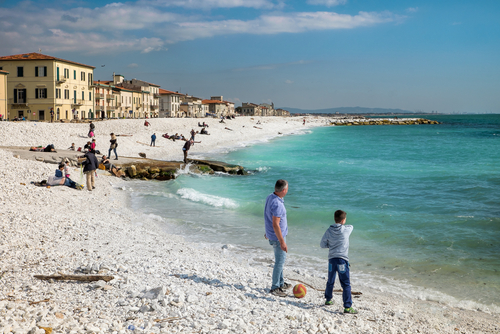 View of the sea and the beach of white pebbles, people take the first sun of the season in Marina di Pisa, Tuscany, Italy