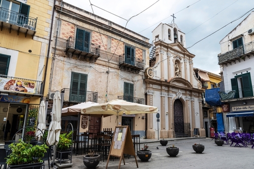 Street of the old town with a terrace of a bar restaurant and a church in the old town of Monreale near Palermo, Sicily, Italy