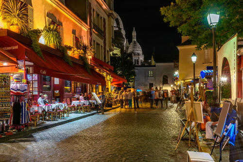 Typical night view of cozy street with tables of cafe and easels of street painters in quarter Montmartre in Paris, France