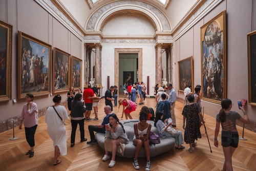 Brightly lit interior of the Louvre Museum in Paris, France, filled with a large group of people