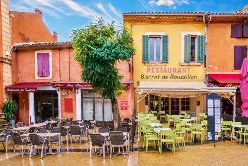 Colorful buildings painted with locally mined ochre pigment. Couleurs: colors. Brasserie: restaurant serving beer. Presses: squeezed fruit juice, Roussillon, Provence, France