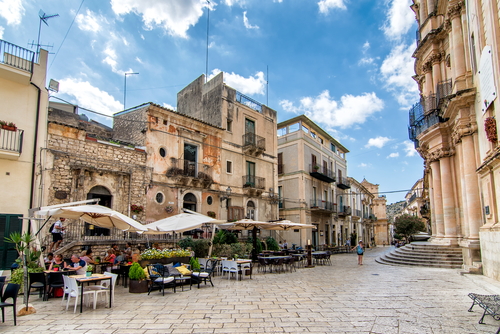People enjoying a cocktail in front of the baroque Church of San Giovanni Evangelista in Scicli, Ragusa, Sicily, Italy