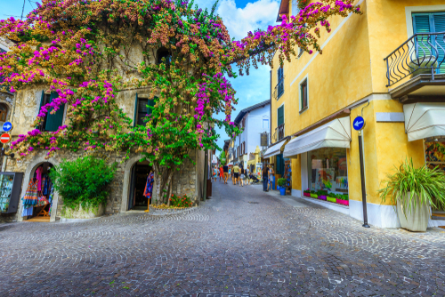 Amazing colorful purple bougainvillea flowers around the windows. Promenade with souvenir shops in Sirmione, La Garda, Italy