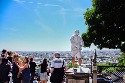 Street performance of actor stylized as sculpture, a living statue on a background of the cityscape. Blue sky. Summer sunny day in Paris, France