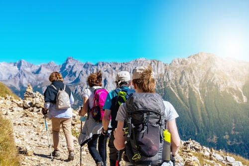 Group of hikers of different gender and age trekking on a trail in the Italian alps, Dolomite peaks of Rosengarten, Catinaccio are visible in the background. Carezza, Val d'Ega, South Tyrol, Trentino Alto Adige, Italy
