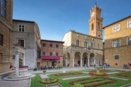 Piazza Pio II., Idyllic square with fountain, town hall and a small coffee house in Pienza. Tourists and local people on the Piazza in the old town of Pienza, Val d'Orcia, Tuscany, Italy