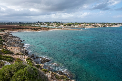 View of the beautiful Ognina beach with turquoise and green water and a small island in front of it near Syracuse, Sicily, Italy