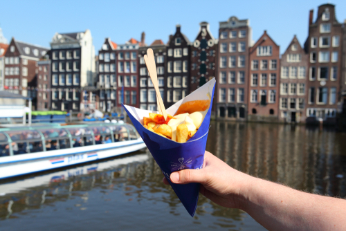 Man holding a paper bag with french fries in the center of Amsterdam, The Netherlands