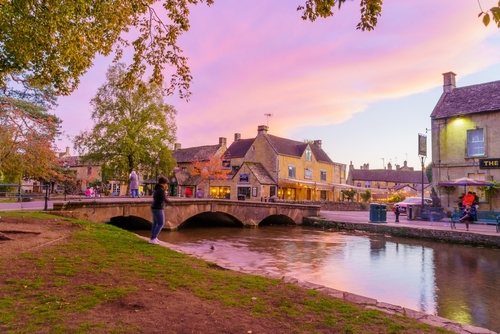 Sunset scene of typical houses, the river Windrush, locals and visitors, in the village Bourton-on-the-Water, the Cotswolds region, Gloucestershire, England, United Kingdom