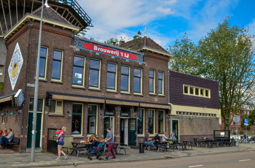 The Brouwerij't IJ brewery is housed in a mill which retains all its original charm. People at the enjoy the excellent artisan beer at the tables. Red brick building, Amsterdam, The Netherlands