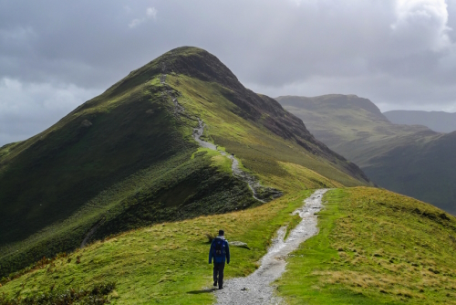 A person walking on the hiking trail in the mountain landscape of Catbells hill top, the Lake District National Park, Cumbria, England, United Kingdom
