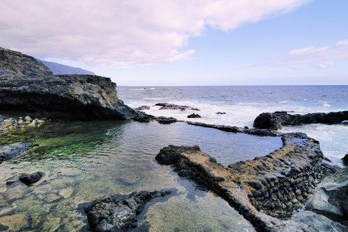 Exterior view of charco azul volcanic cavern, natural volcanic ocean pool with turquoise ocean water, with the Atlantic ocean in the background, Frontera, El Hierro island, The Canaries, Spain