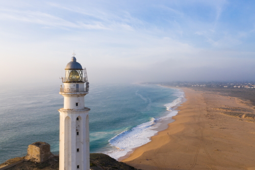 View of the Trafalgar Lighthouse on the Costa de la Luz in Caños de Meca, Cadiz, Andalusia, Spain. Faro de Trafalgar from above on a beautiful day with clouds and the blue sea
