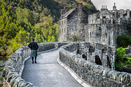 A person wearing a kilt walking towards the Scottish Eilean Donan Castle, Isle of Skye, Scotland, United Kingdom