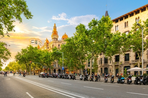 The sun sets on Paseo de Gracia avenue across from the Plaza de Catalunya in the Eixample district with the picturesque Cases Antoni Rocamora building in the sunlight, Barcelona, Catalonia, Spain