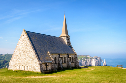 Rear view of Notre-Dame de la Garde on the Amont cliff in Etretat, Normandy, France. With the Aval cliff, its arch and the Needle in the distance on a sunny spring day