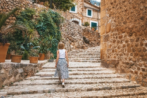 Woman going up the steps in the cozy street of a small village Fornalutx on Mallorca island, Balearic Islands, Spain
