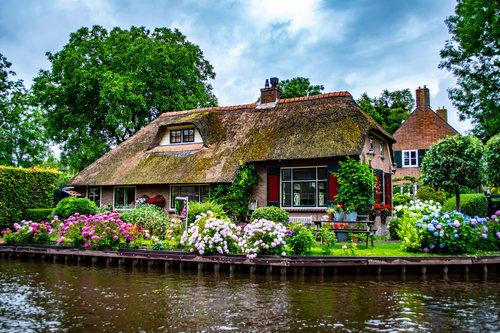 Beautiful Dutch brick house with traditional roof in the village of Giethoorn and beautiful colorful flowers, a famous tourist destination near Amsterdam, The Netherlands