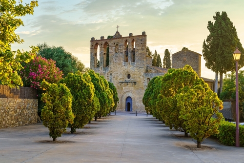 Old stone church with walk with trees at sunset in the town of Peratallada, Girona, Catalonia, Spain