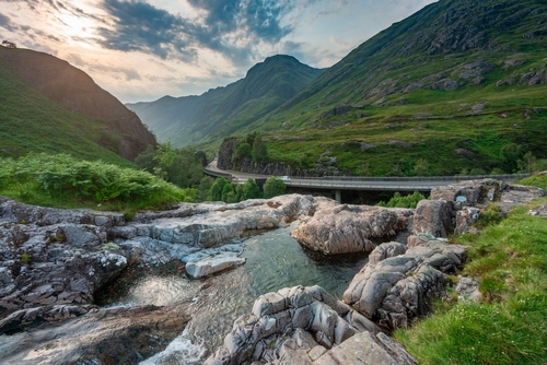 The setting sun, over the dramatic valley of Glen Coe, in Summertime, where three small rivers meet at the foot of the Three Sisters of Glen Coe, Lochaber, Highlands, Scotland, United Kingdom