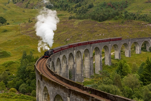 Crowds of people gather to watch the traditional Jacobite Steam Train crossing the famous viaduct at Glenfinnan in the Scottish Highlands, Scotland, UK