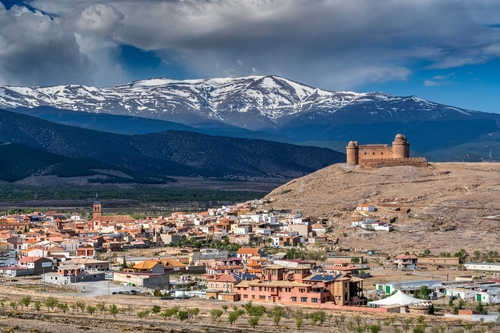 View of the La Calahorra town and castle with the snow-capped Sierra Nevada Mountain Range in the background, Andalusia, Spain