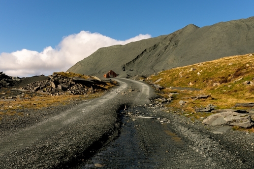 The mining road leads to an old, corrugated, tin shack, rusting away as it slowly merges into the mountain of spoil from the slate mine. High up in the fells above Honister Pass in the Lake District National Park, Cumbria, England, United Kingdom