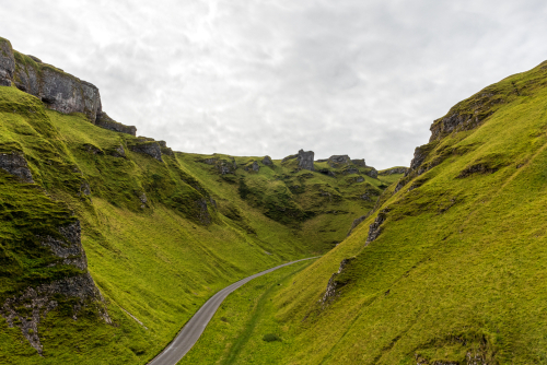 A road cuts through alien-like hills covered in lush green vegetation known as Dark Peak on a cloudy day in the Peak District National Park, Derbyshire, England, UK