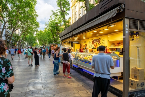 Tourists line up at an outdoor gelateria ice cream kiosk on the famous La Rambla street in the historic center of Barcelona, Catalonia, Spain
