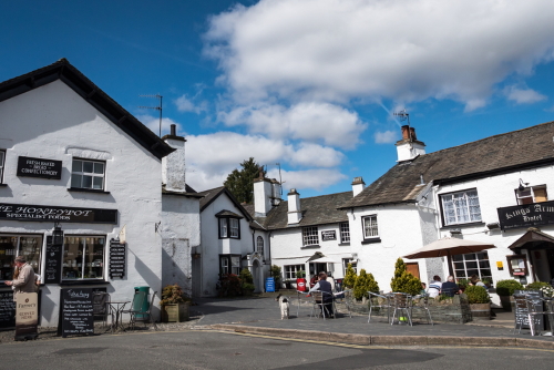 The popular village of Hawkshead in the heart of the English Lake District National Park with tourists outside a small business shop and hotel, Cumbria, England, United Kingdom