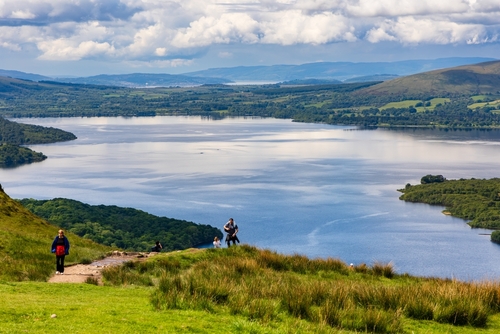 Hikers and walkers descending Conic Hill overlooking Balmaha and Loch Lomond in the Scottish Highlands, The Trossachs National Park, Highlands, Scotland, UK