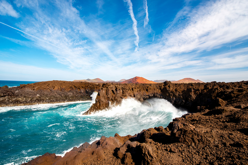 Los Hervideros rocky coast with wavy ocean and volcanos on the background on Lanzarote island, The Canary Islands, Spain