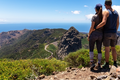 Couple with scenic view from Mirador Morro de Agando on mountain road next to volcanic rock formation Roque de Agando in Garajonay National Park, La Gomera Island, The Canary Islands, Spain