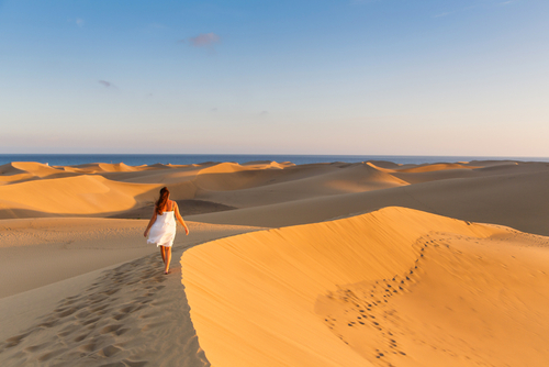 Young beautiful woman walking on the sand wearing white dress at Maspalomas dunes beach, Gran Canaria Island, The Canary Islands, Spain