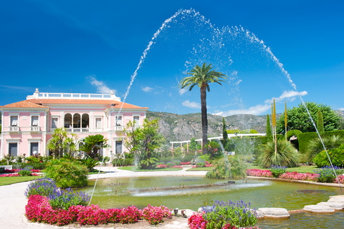 Saint Jean Cap Ferrat, view of the landmark Villa and Jardins Ephrussi de Rothschild, a historic luxury villa with beautiful gardens between Nice and Monaco. Mediterranean garden with fountain, colorful flowers and blue sky. Nice, Cote d'Azur, France