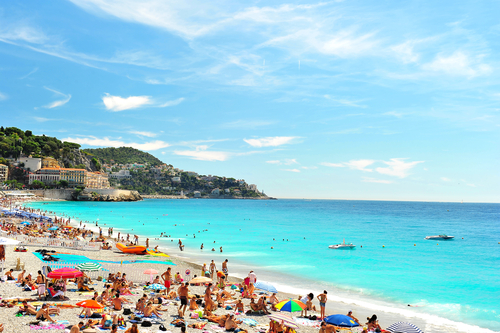 View of the beach in Nice, Cote d'Azur, France, near the Promenade des Anglais. tourists, sunbeds and umbrellas on summer hot day