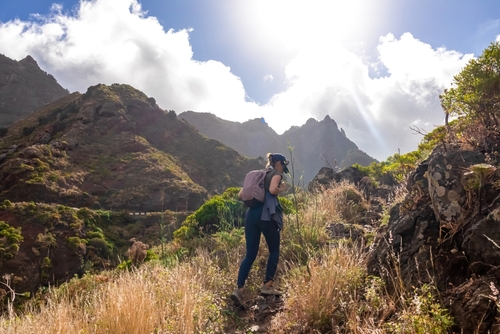 Woman with backpack walking on a panoramic hiking trail in the mountains of Anaga massif between Afur and Taganana in Park Rural de Anaga Mountains, Tenerife island, The Canary Islands, Spain
