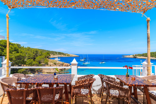 Tables with chairs on terrace of coastal restaurant in Cala Portinatx bay, Ibiza island, Balearic Islands, Spain