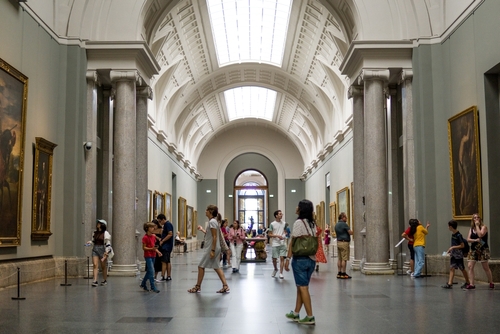 Tourists wandering through the central corridor of the Prado Museum observing famous paintings in Madrid, Spain