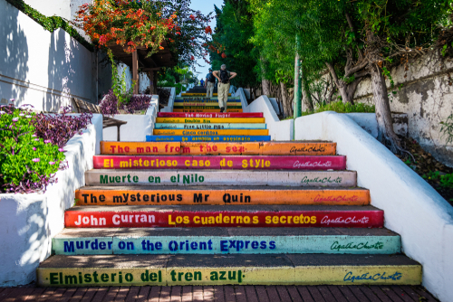 Elderly tourist couple climb colorful stairs with Agatha Christie´s book titles written on them in Puerto de la Cruz, Tenerife Island, Canary Islands, Spain