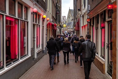 Tourists walking in the red light district, where prostitutes try to lure customers from behind their windows, Amsterdam, The Netherlands